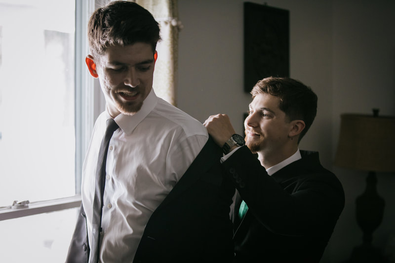 best man helps groom put on jacket in grooms room