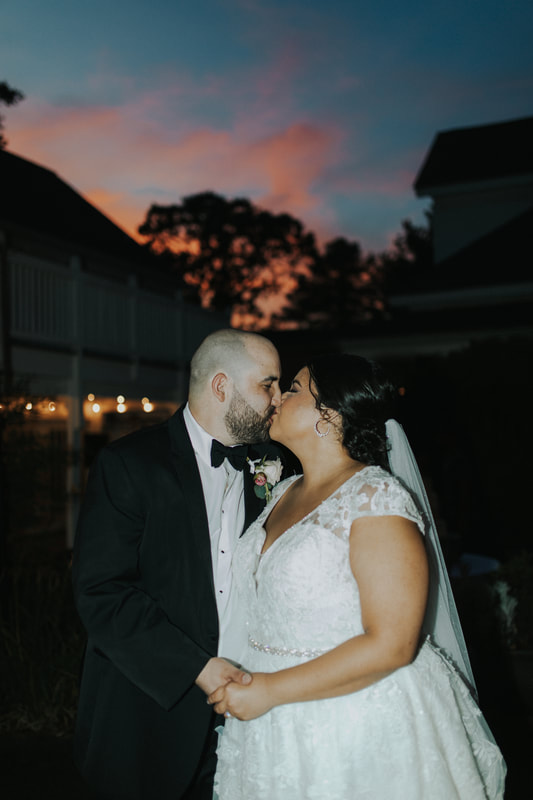 bride and groom kissing at outdoor venue with sunset in background