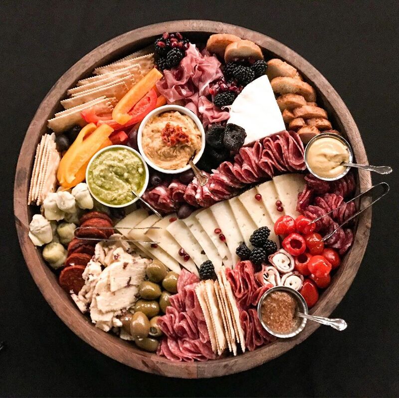 A round charcuterie board filled with an assortment of cheeses, meats, olives, berries, vegetables, and dips.