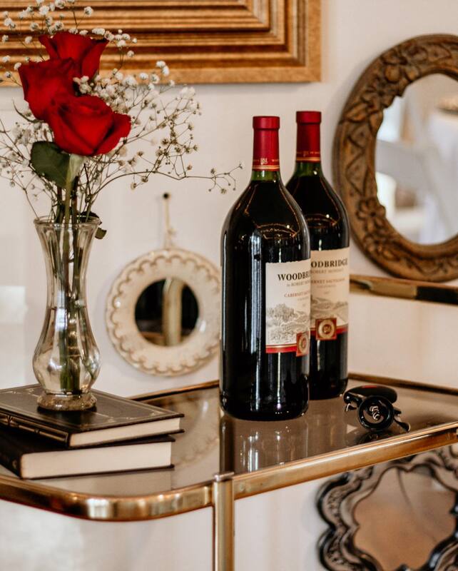gold bar cart with red wine bottles and vase on top of vintage books