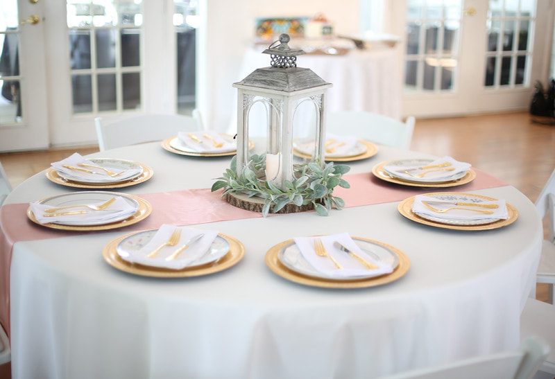 table setup for girl baby shower with pink runner, gold place settings, and ash grey lantern