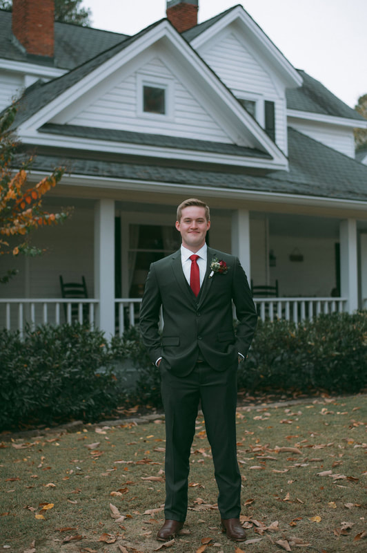 groom in charcoal suit in front of white farmhouse porch
