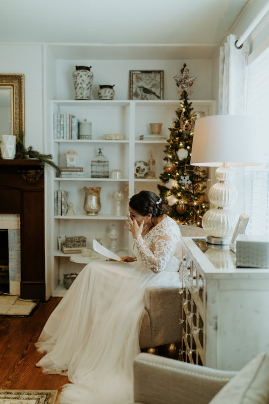 bride wiping away tear while reading letter from groom and sitting in Christmas decorated farmhouse bridal suite