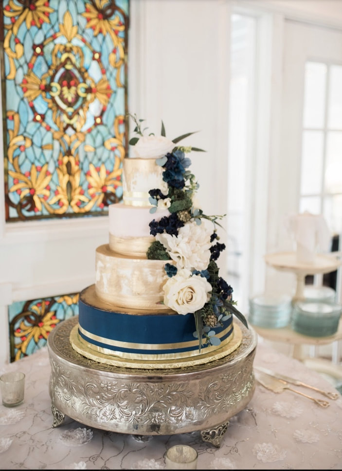 modern wedding cake with navy, gold and champagne accents with white and blue flowers and eucalyptus decorating cake