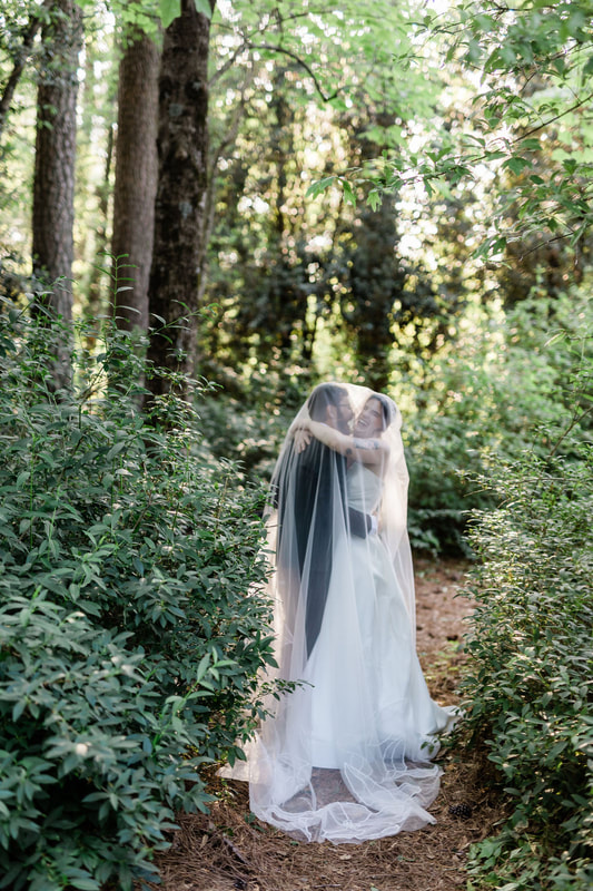 bride and groom hugging under veil standing between bushes