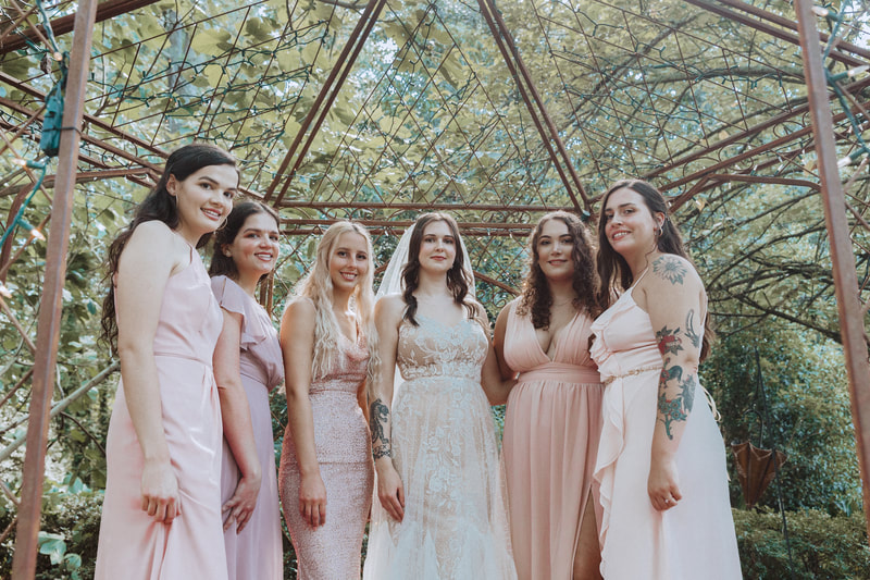 bride with bridesmaids in blush and pastel dresses posing in gazebo