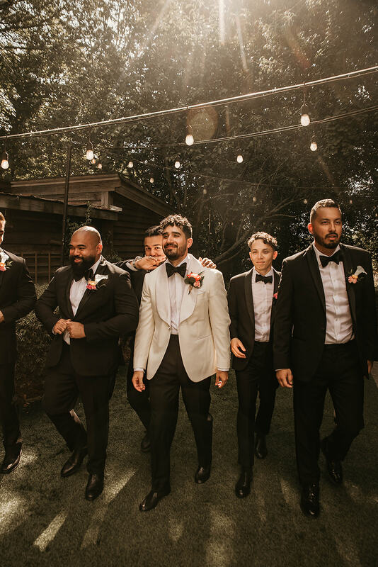 groom in white jacket walking with groomsmen in black suits in farmhouse backyard