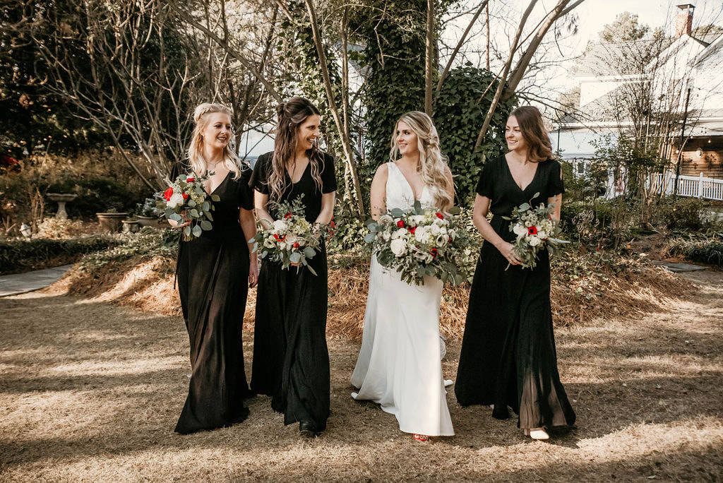 Bride with her bridesmaids wearing black bridesmaids dresses at an outdoor garden venue. 