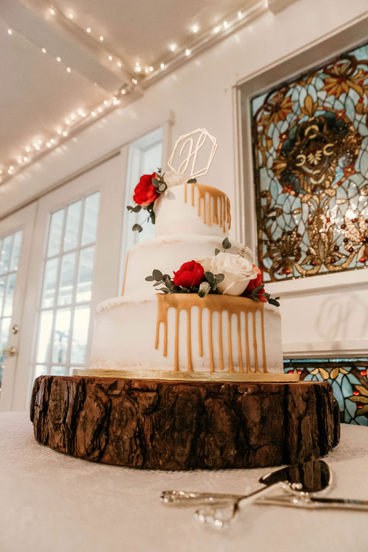 Winter white wedding cake with red and white roses and a caramel dripped icing on a wood slice. 